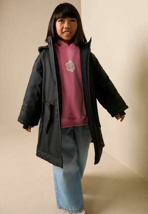 Sort puffervest med hætte over en lyserød hættetrøje med blomsterdesign, sat sammen med blå vidbenede jeans. Afslappet vinteroutfit.