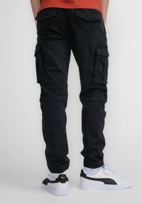 Zwarte cargobroek met meerdere zijzakken, een tapered fit en elastische boorden. Gecombineerd met witte sneakers met zwarte accenten.