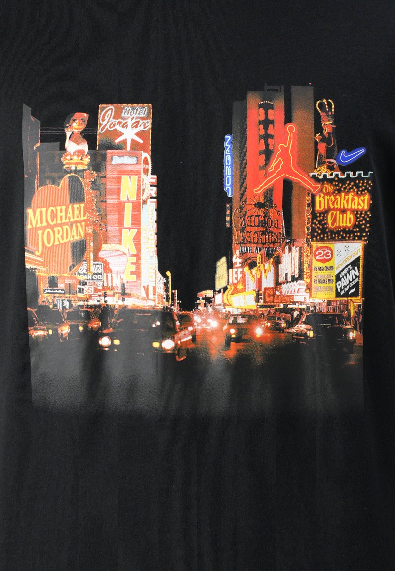 Czarna koszulka z kolorową grafiką przedstawiającą miejską scenę z neonowymi znakami, samochodami i światełkami miasta, podkreślająca marki takie jak Nike i Michael Jordan.