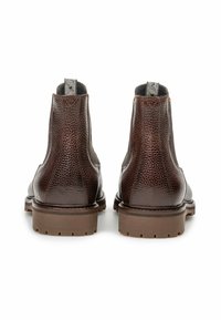 Botas de cuero marrón hasta el tobillo con un acabado texturizado, que presentan una suela de goma y lengüetas de agarre con un patrón en contraste.