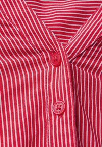 Red and white striped fabric with a collar, featuring two red buttons. The texture appears soft and the stripes are evenly spaced.