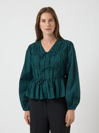 Blusa lunga color teal con scollatura a V, texture arricciata e orlo a peplum. Presenta dettagli con cordoncino sul davanti.