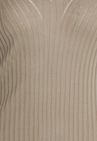 Tissu en tricot côtelé beige avec un motif à rayures verticales et un bord festonné le long du centre supérieur.