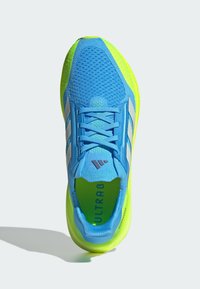 Zapatilla deportiva azul con parte superior de malla, acentos en verde brillante, tres rayas blancas y la marca 'ULTRABOOST' en la plantilla.
