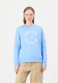 Lyseblå hettegenser med rund hals, ribbestrikkede mansjetter og kant. Har trykt tekst i rosa og hvitt: "TOMMY JEANS NEW YORK CITY" med hjerter.