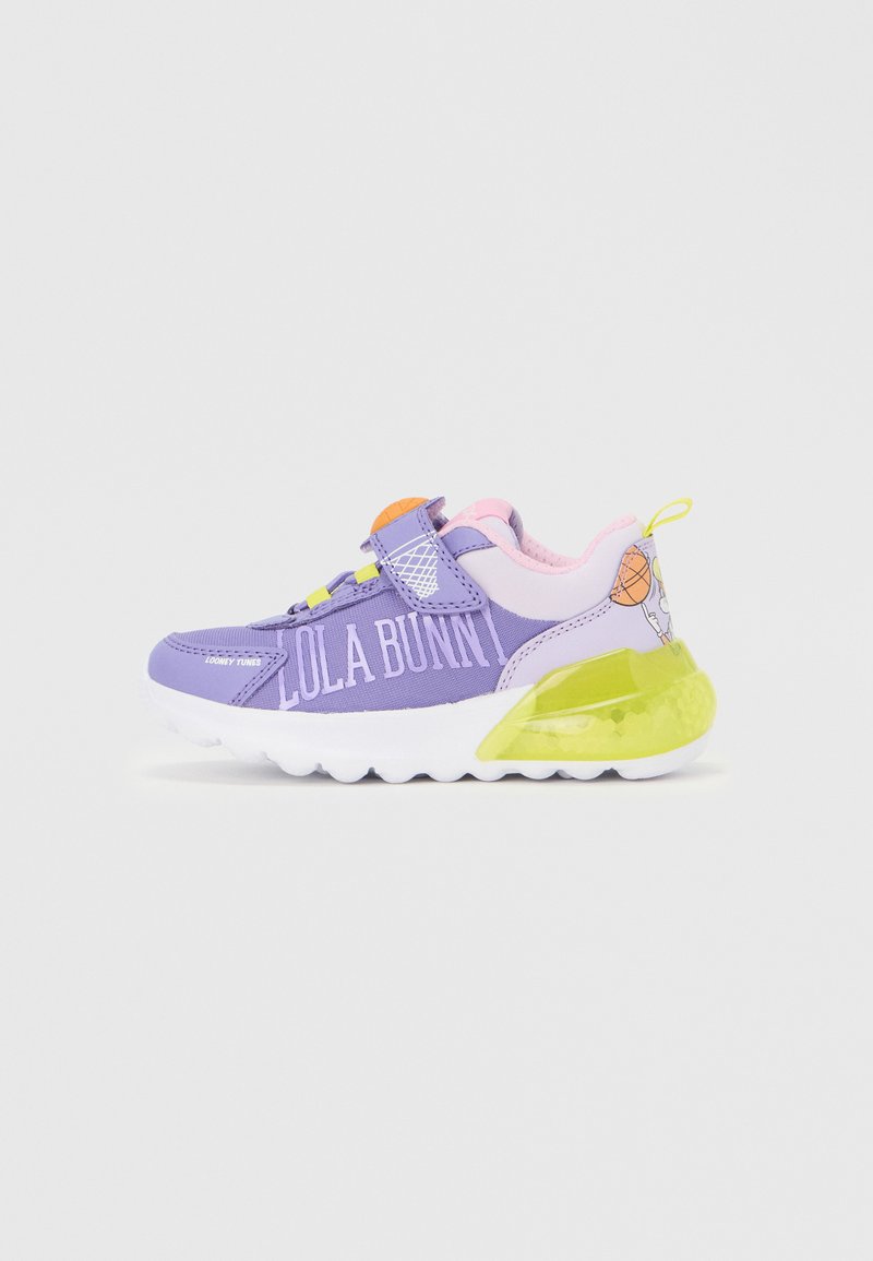 Zapatillas deportivas moradas con una tira de velcro, detalles en tonos pastel, un talón verde translúcido y "LOLA BUNNY" impreso en el lateral.