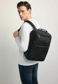 Czarny plecak wykonany z trwałej tkaniny, wyposażony w wiele zamykanych na zamek przedziałów, wyściełane paski i górny uchwyt. Prosty, prostokątny kształt.