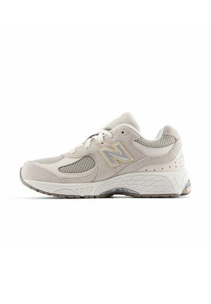 Light beige athletic shoe made of mesh and suede, featuring a textured sole, padded collar, and a silver-gray New Balance logo.