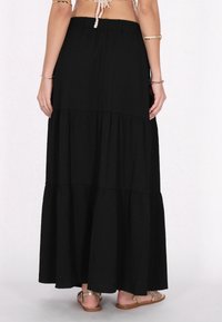 Zwarte maxi-rok met gelaagd ontwerp, textuurstof en een elastische tailleband. Draag met gouden platte sandalen.