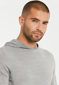 Grijze hoodie met een zachte textuur, voorzien van een trekkoordcapuchon en geribbelde accenten bij de hals. Close-up van het bovenlichaam.
