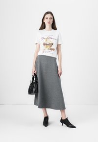 White cotton t-shirt with graphic dessert print, paired with a long grey skirt. Accessories include a black handbag and black pointed shoes.