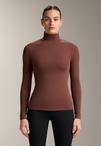 Brun långärmad polotröja i mjukt, stretchigt material. Figursydd design med hög krage. Kombinerad med svarta leggings.