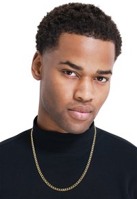 Collier en chaîne dorée avec des maillons épais, port�é sur un col roulé noir. Le sujet a les cheveux courts et bouclés et une expression neutre.