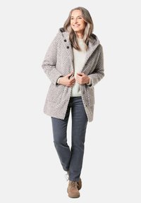 Manteau à capuche gris texturé avec de gros boutons, porté sur un pull léger et un pantalon sombre, associé à des bottes en cuir à lacets marron.