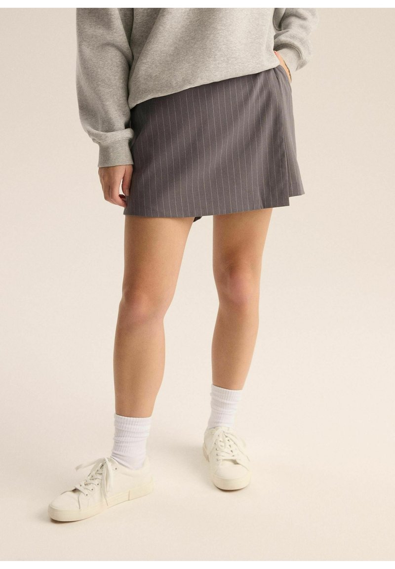 Szara spódnica w paski z rozkloszowanym dołem, zestawiona z szarym swetrem i białymi trampkami, z prążkowanymi białymi skarpetkami.