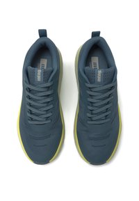 Zapatos deportivos de color verde oscuro con parte superior de malla transpirable, cordones grises y suela de un amarillo brillante. Cuenta con un collar almohadillado y un logo en la lengüeta.