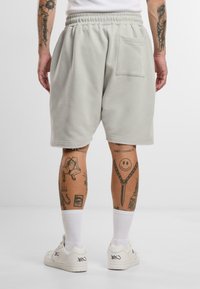 Lysegrå bomullsshorts med elastisk midje, med en baklomme. Brukt med hvite joggesko og stripete hvite sokker.