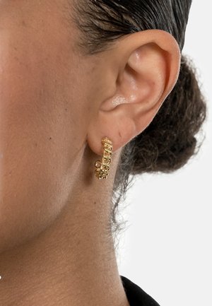 Gold hoop earring with chain-link design, features textured surface, small floral accent, and a shiny finish. Placed on a model's ear.