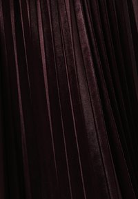 Donkerbordeaux geplooide stof met een gladde, fluweelachtige textuur. Verticale plooien creëren een gestructureerd, gelaagd ontwerp.