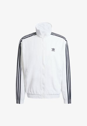 Chaqueta blanca con cierre en la parte delantera y cuello alto, con acentos en negro de tres rayas en las mangas y un pequeño logo negro de adidas en el pecho.