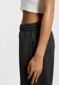 Pantalons de training noirs avec une taille élastique texturée et des poches latérales. Le matériau semble doux et légèrement chiné dans sa finition.