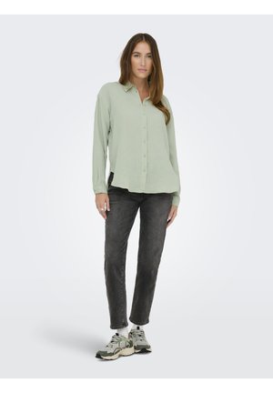 Light green, button-up shirt in a textured fabric, paired with dark grey jeans. Model wears grey and green sneakers with white socks.