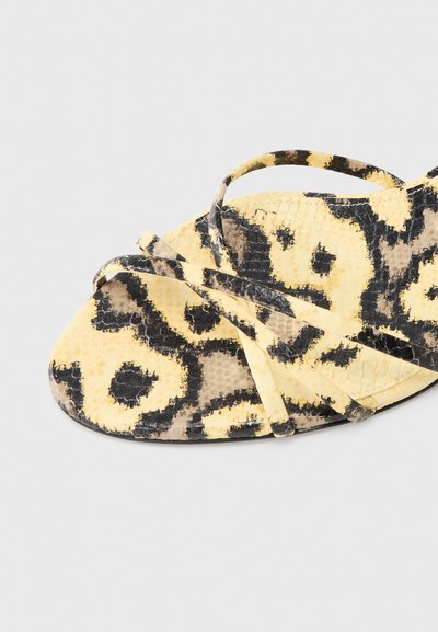 Κίτρινα και μαύρα σανδάλια με σχέδιο που μοιάζει με δέρμα φιδιού. Διαθέτουν σταυρωτά λουριά και επίπεδη σόλα.