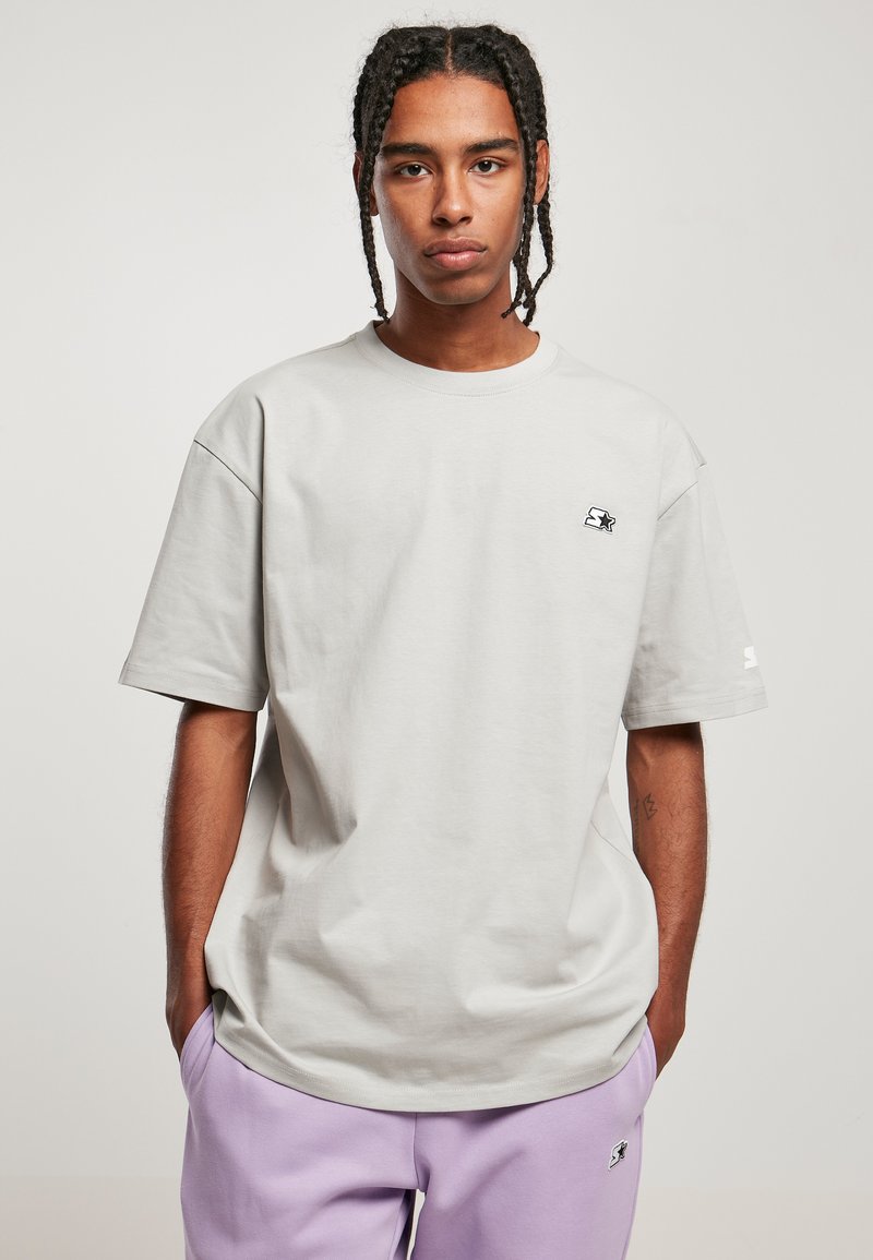 Světle šedé oversized tričko vyrobené z bavlny. Má krátké rukávy, kulatý výstřih a malé potištěné logo na levé hrudi.