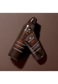 Bruna rakgel- och balmbehållare med vita och oranga textetiketter, utrustade med ett rundat korklock och en slät yta.