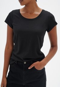 Černé krátké tričko s měkké látky s kulatým výstřihem, v kombinaci s černými džíny. Tričko má slim fit a jednoduchý design.