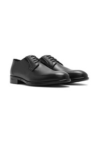 Chaussures noires en cuir à lacets avec une texture lisse, un bout arrondi et un design discret. Elles présentent un petit talon et un marquage minimal.