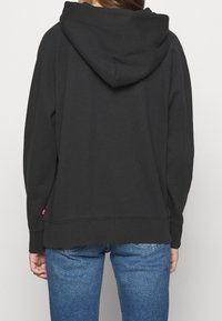 Svart huvtröja med avslappnad passform, mjuk textur, med en känguruficka och ribbade ärmslut. Kombinerad med blå jeans.