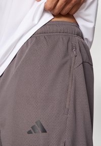 Szare sportowe szorty z siateczki z elastycznym pasem i boczną kieszenią na suwak. Na lewej nogawce znajduje się czarne logo adidas.