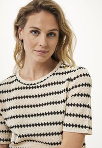 Top in crema a maglia con strisce nero a zigzag, scollatura rotonda, maniche corte e dettagli con bottoni dorati sulle spalle. Tessuto testurizzato.