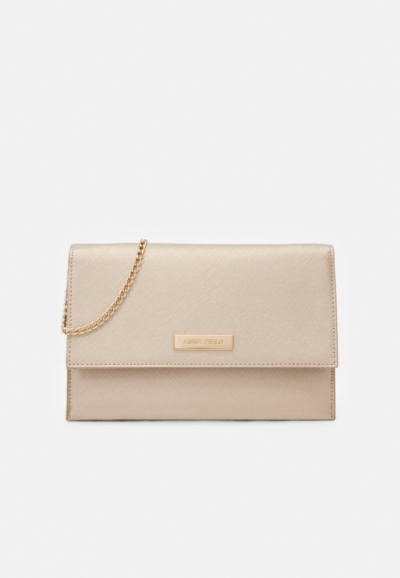 Pochette rectangulaire beige avec finition texturée, bandoulière chaîne dorée et petite plaque métallique rectangulaire avec "ANNA FIELD" embossé.