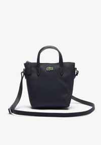 Sac à main bleu marine en matériau texturé avec deux poignées courtes et une bandoulière détachable. Présente un petit emblème de logo sur le devant.