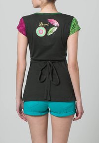 Černý krátký rukáv top se vzorovanými zelenými a růžovými rukávy, detailem zavázání v pase a barevnými prvky na zádech. Kombinováno s tyrkysovými šortkami.