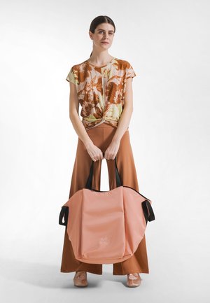 Grote roze draagtasje met zwarte handvatten, gemaakt van zacht materiaal, met een afgeronde vorm en een subtiel logo aan de voorkant.