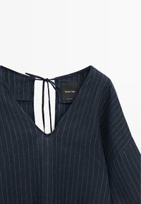 Blouse bleu foncé à fines rayures avec col en V et fermeture par nouage dans le dos, montrant l’étiquette de la marque Massimo Dutti.