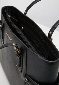 Sac fourre-tout en cuir noir avec quincaillerie dorée, présentant une surface texturée, des anses supérieures doubles et plusieurs compartiments intérieurs.