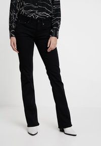Jeans de mezclilla negros con un corte recto, que cuentan con cinco bolsillos y un ligero estiramiento. Llevados con una blusa de estampado en blanco y negro.