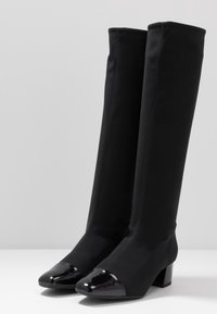 Knöchelhohe schwarze Stoffstiefel mit spitzen Zehen aus Lackleder und Blockabsätzen. Mit sichtbaren Nähdetails.