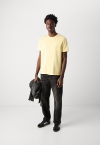 Yellow cotton t-shirt with short sleeves and subtle branding, paired with dark denim jeans and black leather jacket. Black sneakers with white accents.