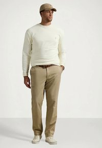 Lysebeige crewneck-genser, khakibukser, matchende caps, hvite joggesko; avslappet passform med en subtil logodetalj på genseren og buksene.