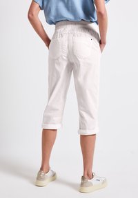 Witte cropped broek met een elastische tailleband, opgerolde boorden en twee achterzakken. Gemaakt met witte en beige sneakers.