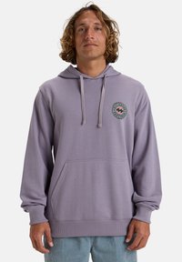 Felpa lilla realizzata in tessuto morbido, con tasca a marsupio, cappuccio regolabile con cordini e una patch a logo circolare sul petto.