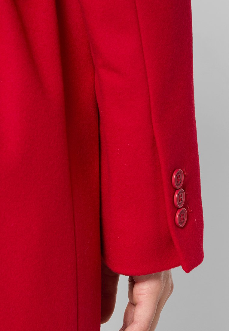 Manica di un cappotto rosso di lana con una texture liscia e tre bottoni rotondi rossi abbinati al polsino. Design semplice, vestibilità su misura.
