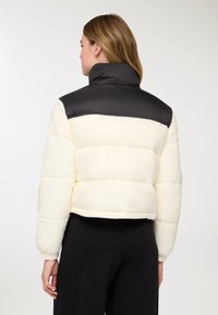 Piumino con corpo color crema e colletto nero, design corto con imbottitura trapuntata e polsini elasticizzati per una vestibilità aderente.