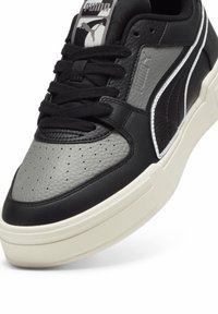 Gros plan d'une basket Puma noire et grise en cuir texturé, lacets noirs, semelle blanche et logo Puma sur la languette et le côté.