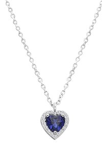 Un collar con colgante en forma de corazón presenta una gema azul profunda rodeada de pequeñas piedras transparentes, sobre una cadena de eslabones en tono plateado.